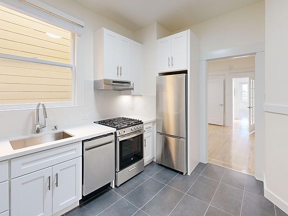 Kitchen with multiple cabinets, refrigerator, stove, range hood, and sink