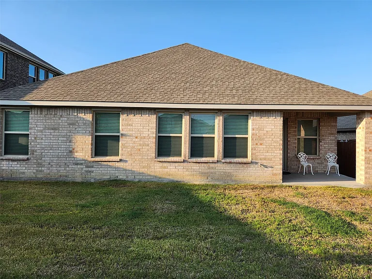 Light-colored brick exterior featuring multiple windows with blinds, a covered patio area, and an expansive lawn