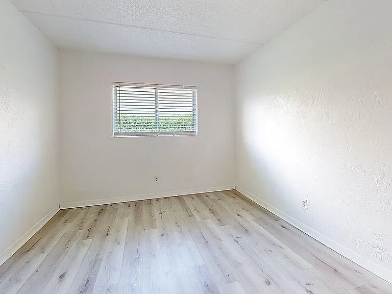 Bright and airy room with fresh white walls and elegant wood flooring, featuring a large window inviting ample natural light.