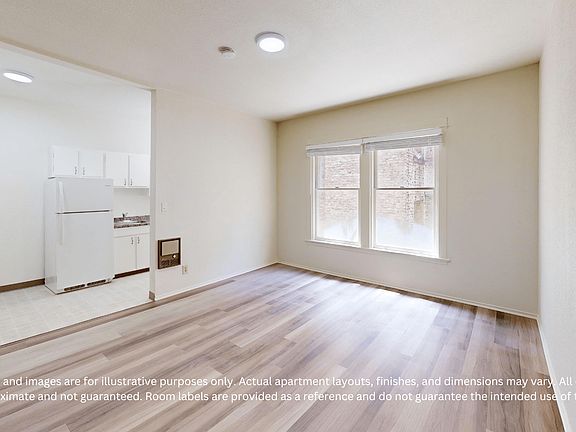 Bright, empty apartment with wood flooring and large windows. Adjacent small kitchen with cabinets and appliances. Inviting and spacious.