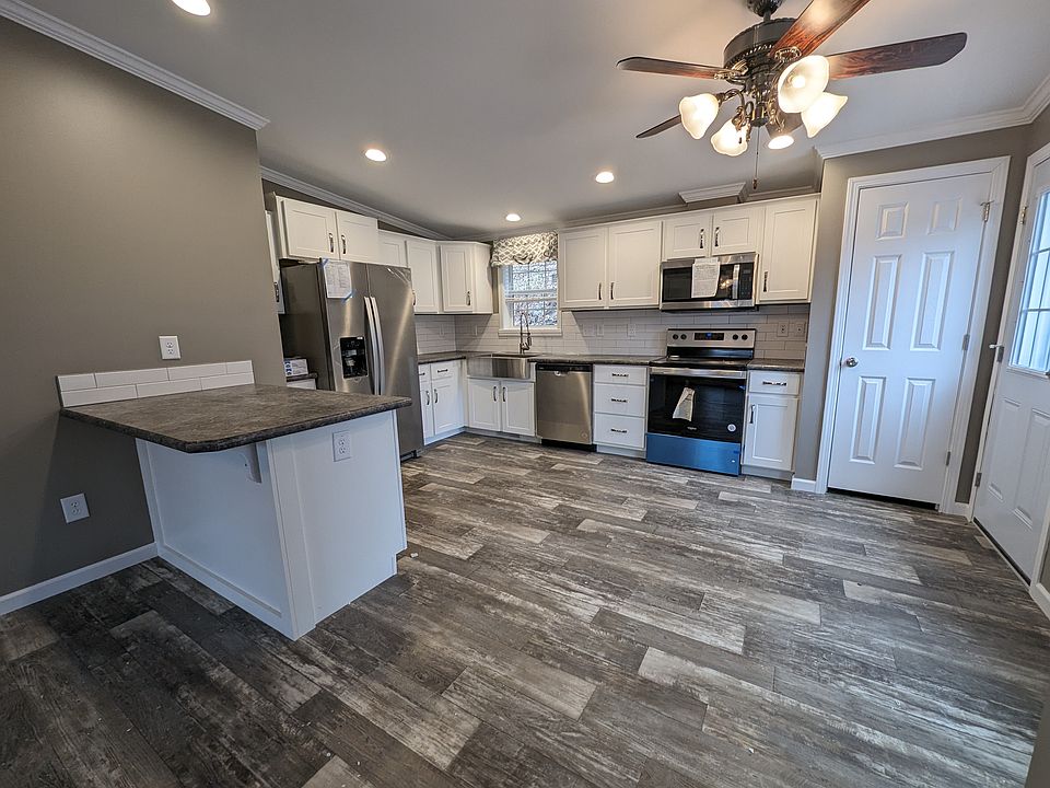 Kitchen with barn style sink and window above with light, peninsula, dishwasher, electric range, microwave and side by side fridge with ice maker and pantry.