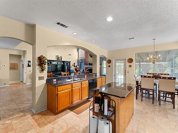 Kitchen featuring black dishwasher, a textured ceiling, a chandelier, brown cabinetry, and arched walkways