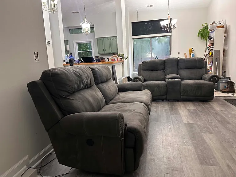 Step into a bright and inviting living space featuring soaring vaulted ceilings and a floor-to-ceiling stone fireplace that serves as the heart of the home. The spacious open-concept layout seamlessly connects the living room, dining area, and kitchen.