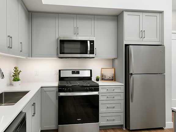 Apartments with modern kitchens featuring grey cabinetry, white quartz stone countertops, white tile backsplash, stainless steel appliances, and hard surface flooring