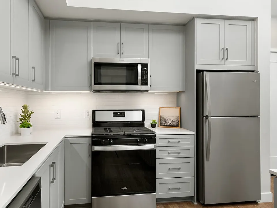 Apartments with modern kitchens featuring grey cabinetry, white quartz stone countertops, white tile backsplash, stainless steel appliances, and hard surface flooring