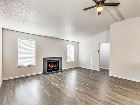 Unfurnished living room with a textured ceiling, a tiled fireplace, dark wood-style floors, and ceiling fan