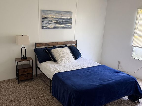 Furnished bedroom with a full bed, nightstand and lamp, plus a window with blinds for comfortable everyday living.