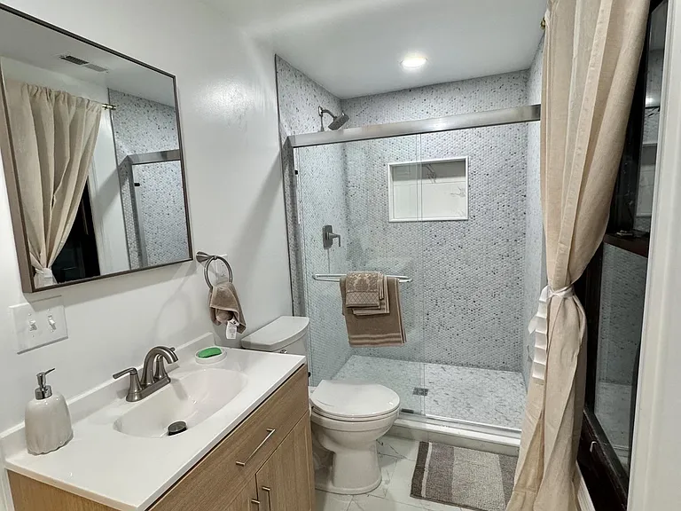 Updated bathroom with single-sink vanity, framed mirror, and a tiled shower with sliding glass door and built-in niche.