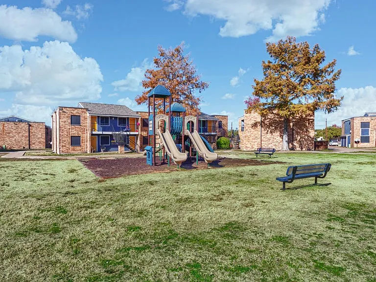 Our community playground offers safe, fun recreation for kids with slides, climbing structures, and benches for parents to relax nearby in a spacious courtyard setting.