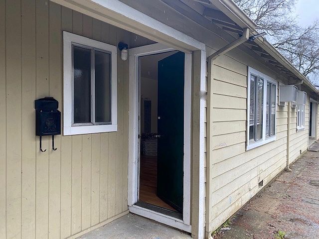 Front door opens to a large living room with a gas wall furnace and an air conditioner. Lots of great natural light