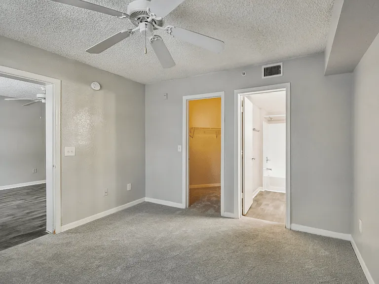 Spacious carpeted primary bedroom with walk-in closet, en-suite bathroom access, and ceiling fan in a 3-bedroom, 2-bath apartment at Gregory Cove in Jacksonville, FL.