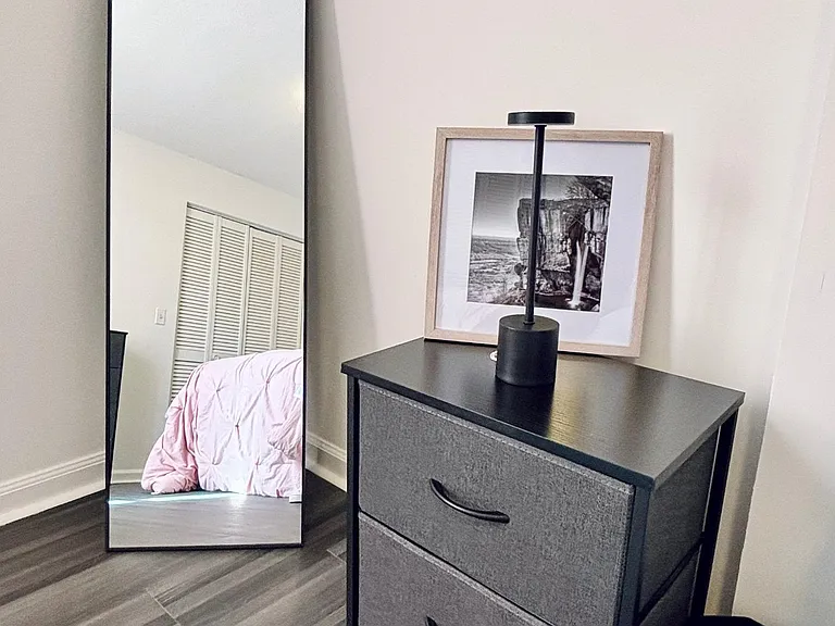 Bedroom corner with durable flooring, a dresser for storage, and a full-length mirror near the closet doors.