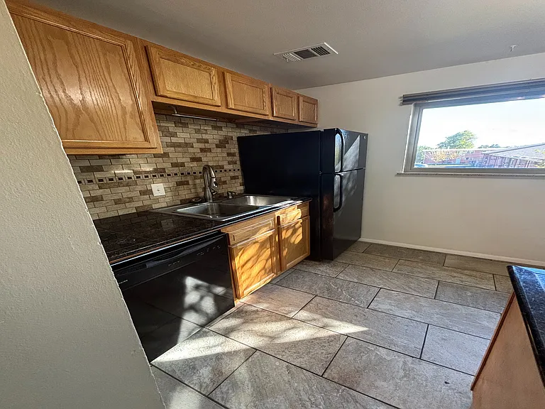 Charming kitchen with warm wooden cabinets, sleek black appliances, and a stylish tile backsplash illuminated by natural light.