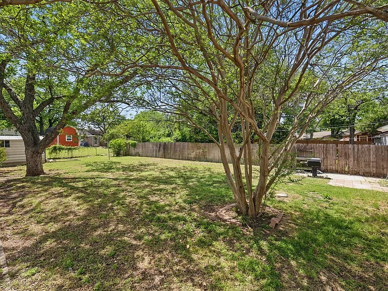 Expansive backyard with a paver patio, established trees providing natural shade, and a storage shed. Grill is non-functioning.