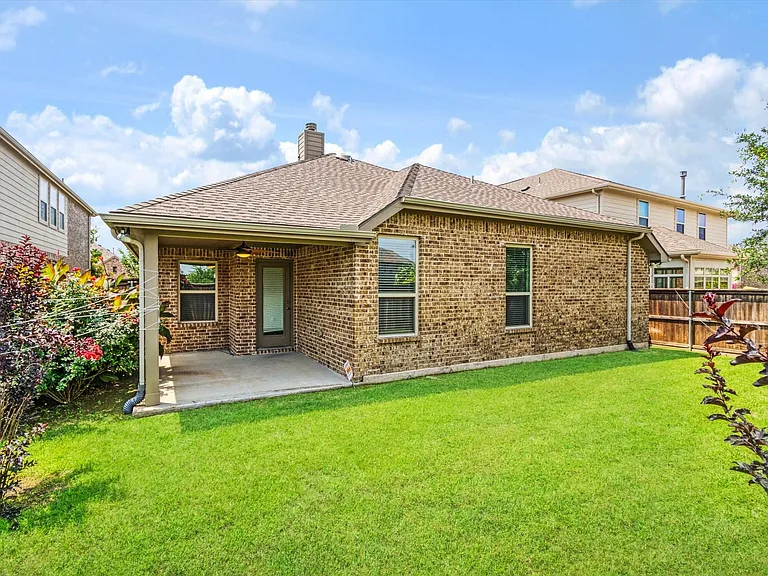 Brick exterior with a covered patio, a well-kept lawn, and mature landscaping