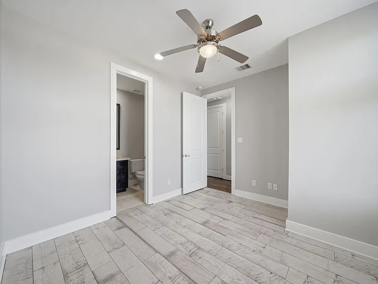 Bright and modern third-floor bedroom featuring light wood flooring, neutral finishes, and a ceiling fan. The space includes a private en-suite bathroom and offers excellent flexibility.