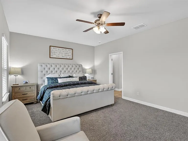 Spacious interior featuring a neutral color palette, ceiling fan with integrated lighting, window with blinds, and durable carpeting