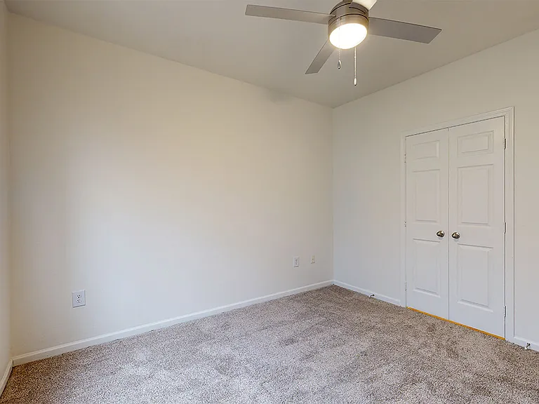 Spacious apartment bedroom with large closet and plush carpet flooring.