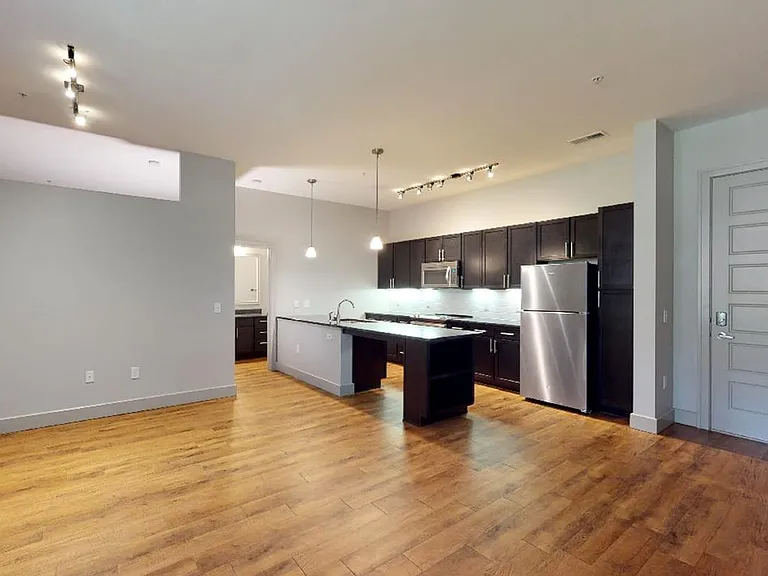 Apartment kitchen with stainless steel appliances, dining and living room with wood-style flooring.
