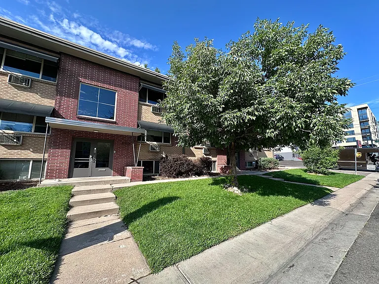 Charming apartment building with a classic brick facade and lush green landscaping, featuring a welcoming entrance and ample natural light.