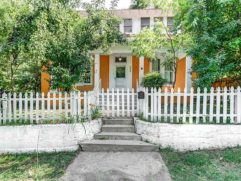 Front of house with fruit trees and a white picket fence.