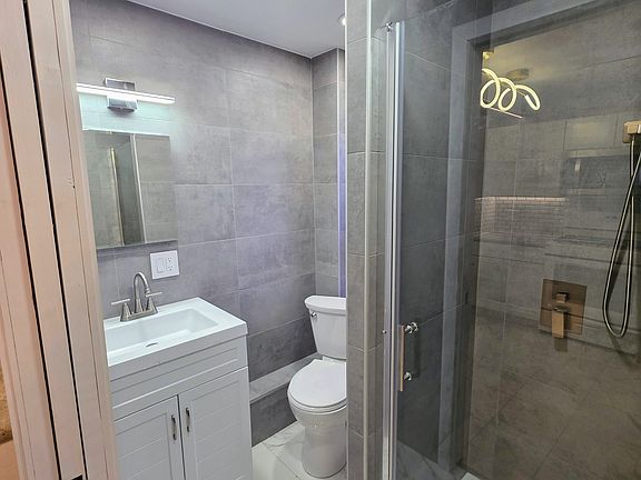 European floor to ceiling tiled bathroom with 2 position shower, LED accent lighting and concealed medicine cabinet.