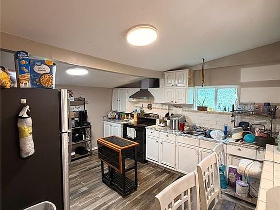 Kitchen featuring wood-finish flooring, white cabinetry, a tile backsplash, and a black range with an overhead hood