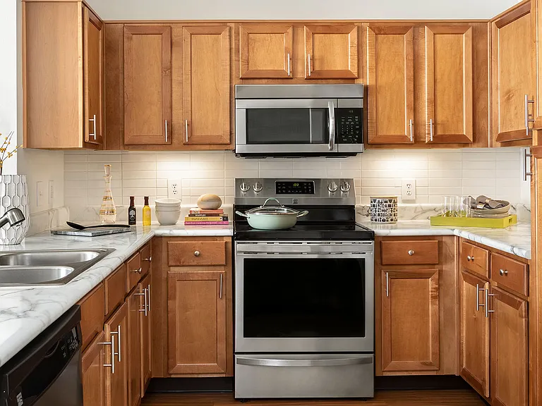 Apartment kitchen with stainless steel appliances, wood-style flooring, and marble-style countertops (shown here). Quartz-style countertops are available in select homes.