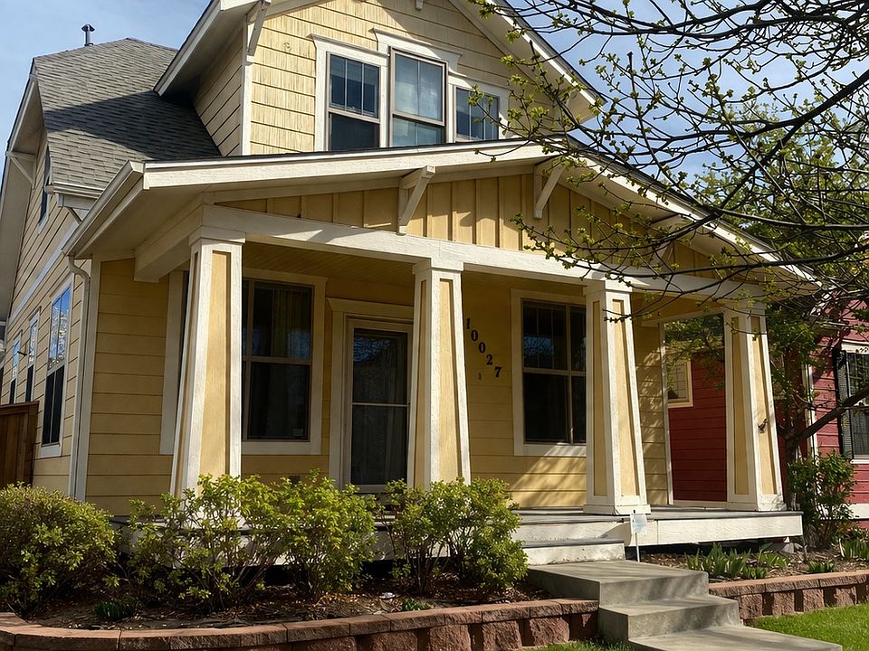 Street view, wide covered porch with craftsman style columns, rose bushes and shade tree.