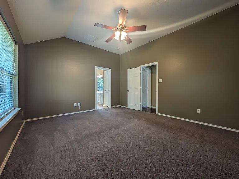 A view showing the generous room dimensions, neutral color palette, and seamless access to both the primary bath and walk-in closet areas.