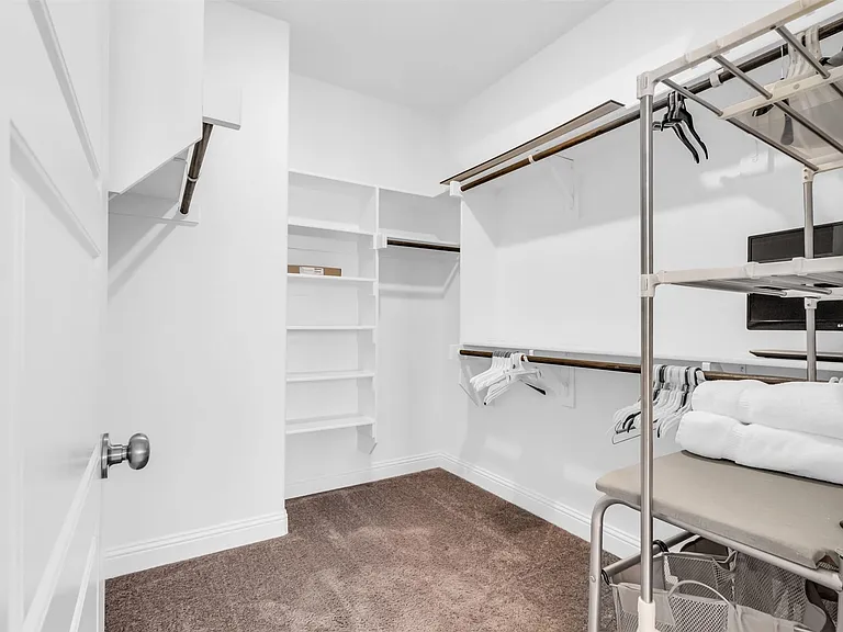 Walk-in closet with carpet flooring, white baseboards, multiple built-in shelving units, and hanging rods