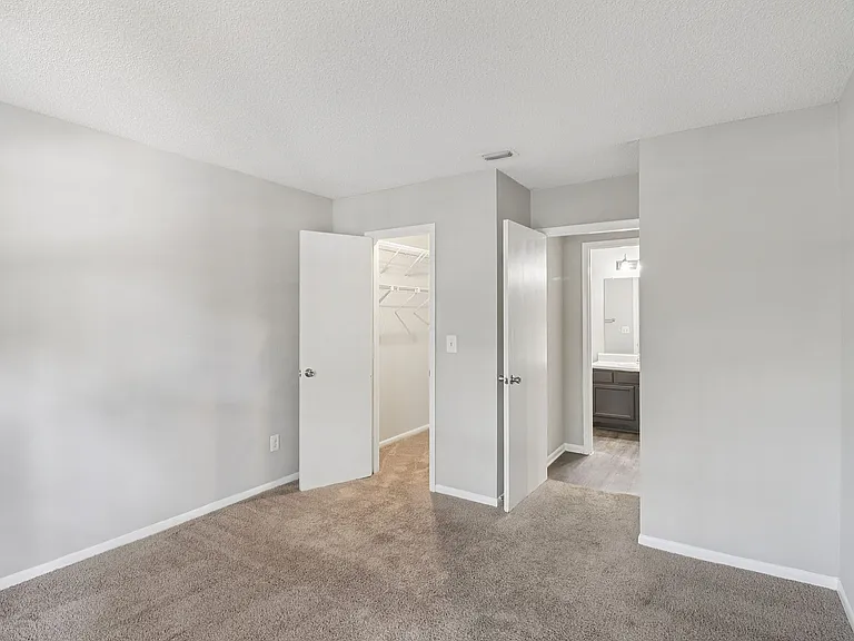 Bright and spacious bedroom with plush carpeting, featuring a walk-in closet and an adjoining bathroom with modern fixtures.
