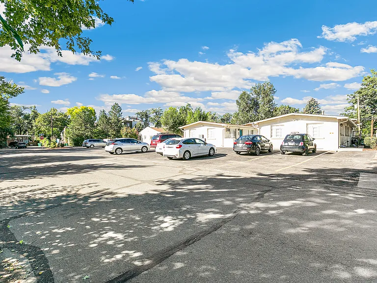 Charming suburban parking area with multiple cars and greenery under a bright blue sky.