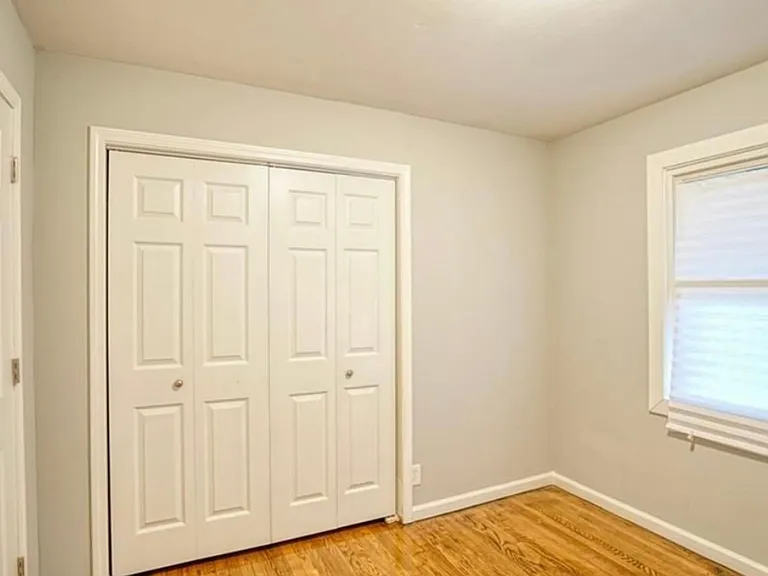 Unfurnished bedroom with hardwood floors, a wide double-door closet, and a window with blinds for natural light.