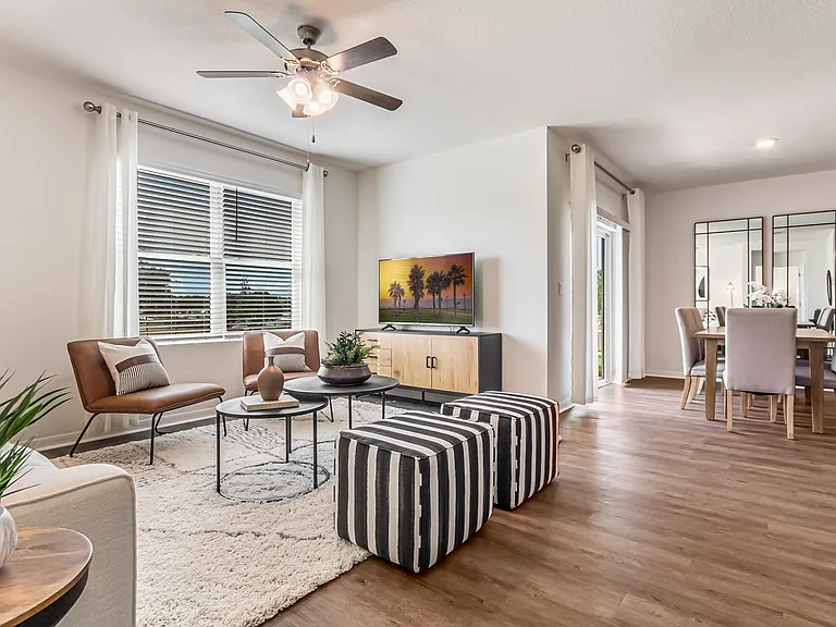 Four-Bedroom Homes for Rent in St. Cloud, FL - Ibis Park at Harmony West - Living Room with Luxury Vinyl Plank Flooring, Area Rug, Couch, Ottoman Stools, Chairs, Multi-Level Coffee Table, Storage Cabinet, TV, Ceiling Fan, Spacious Window, and View of Dini