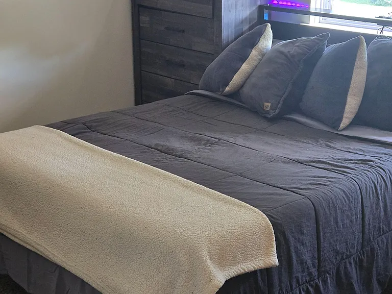 Furnished bedroom featuring a comfortable bed, dresser storage, and a window with blinds for adjustable natural light.