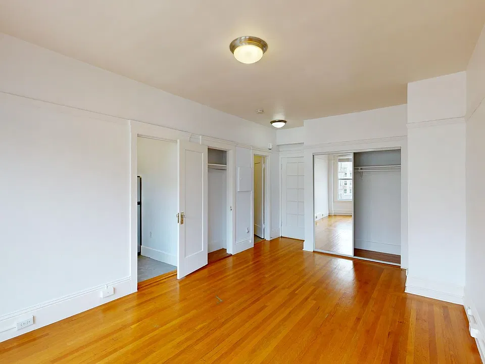 Bright bedroom with wood-like floor, a closet with mirror, and an entrance to the kitchen
