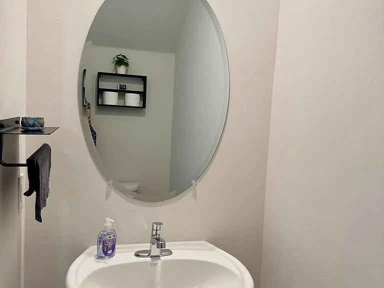 Bathroom vanity area with pedestal sink, oval mirror, and wall shelving for toiletries and linens.