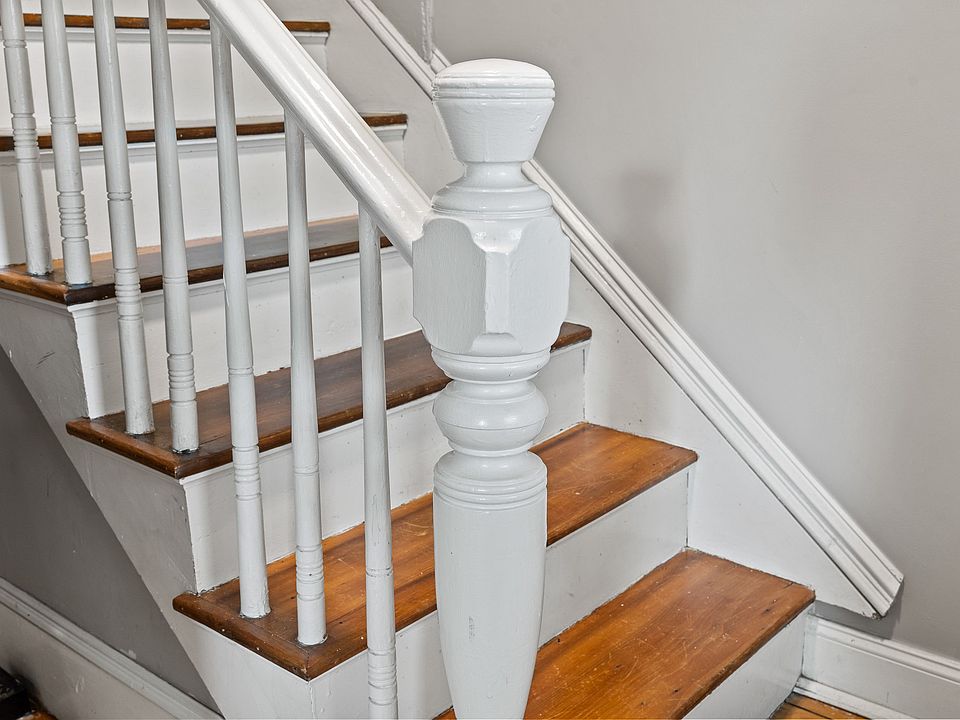 A beautifully maintained traditional staircase leads to the next level. It features a striking contrast between the original, warm-toned wood treads and the crisp white risers, balusters, and newel post. The staircase design adds a touch of classic charm 