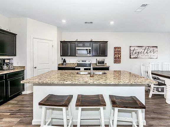 A modern kitchen featuring a large granite island with barstools, dark cabinetry, and an open-concept layout with wood-look flooring.