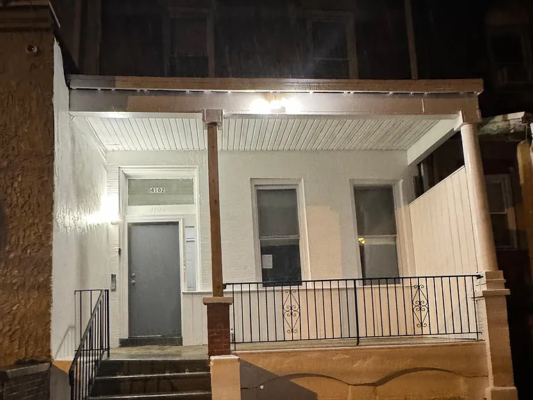 Outside front of building at night has security camera, outside motion light and separate light above the front door
