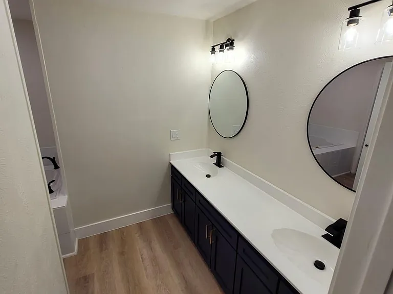 Spacious double-vanity bathroom with two round mirrors, ample counter space, and generous storage cabinetry.