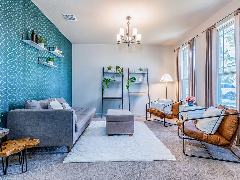 Spacious living room with a large window, comfortable seating area, accent wall, and soft carpet for relaxing or entertaining