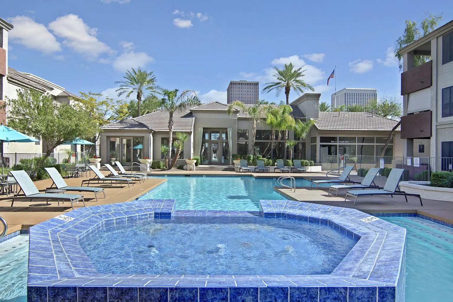 Outdoor swimming pool and spa area with lounge chairs and palm trees.