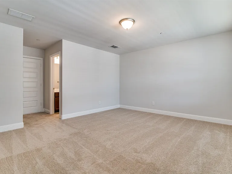 Spacious carpeted room featuring light gray walls, white baseboards, and a semi-flush mount ceiling light fixture