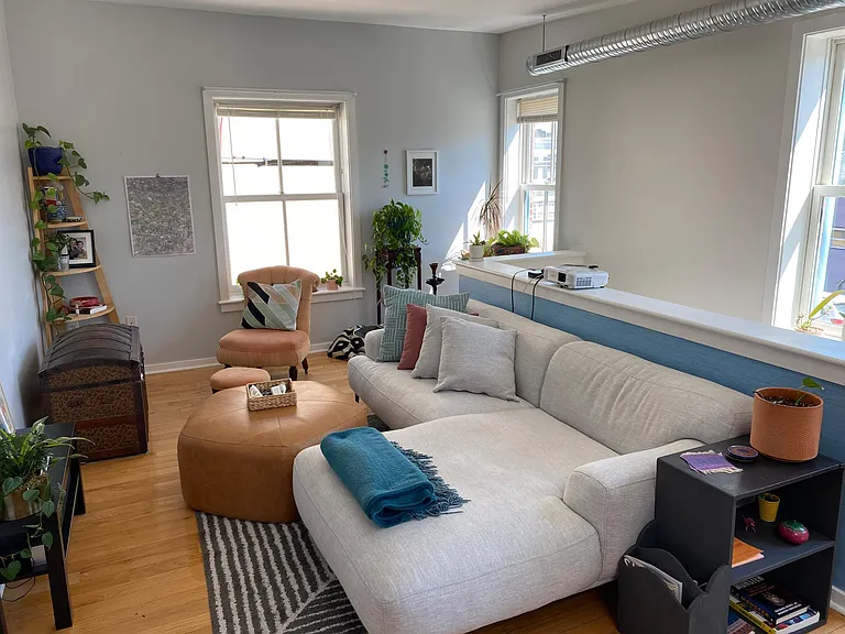 Living area with stairway behind the sofa wall, window faces back alley with brick rowhome wall.