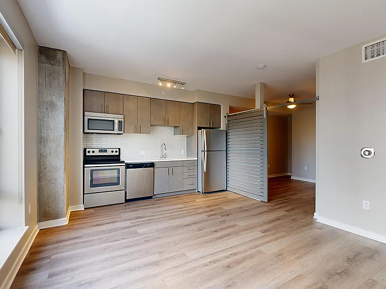 Apartment kitchen with stainless steel appliances, dining and living room with wood-style flooring.