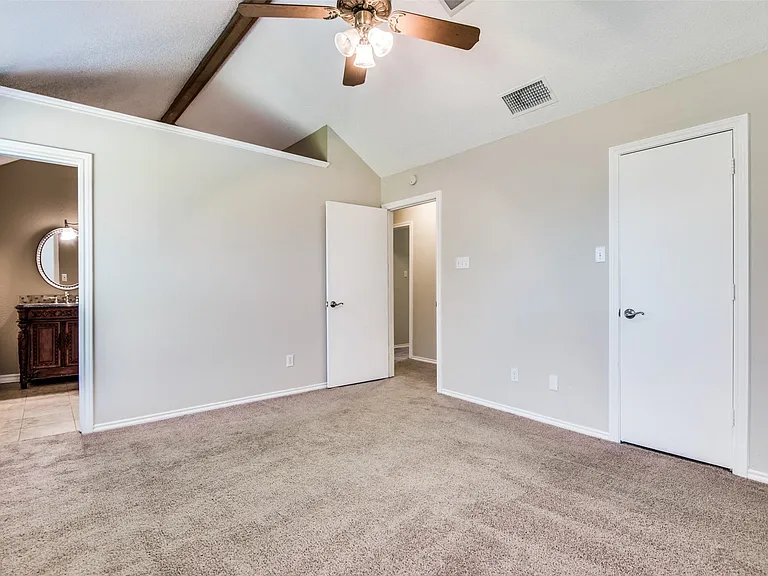 Spacious bedroom featuring vaulted ceilings with exposed wood beams, a ceiling fan with integrated lighting, and plush carpet flooring