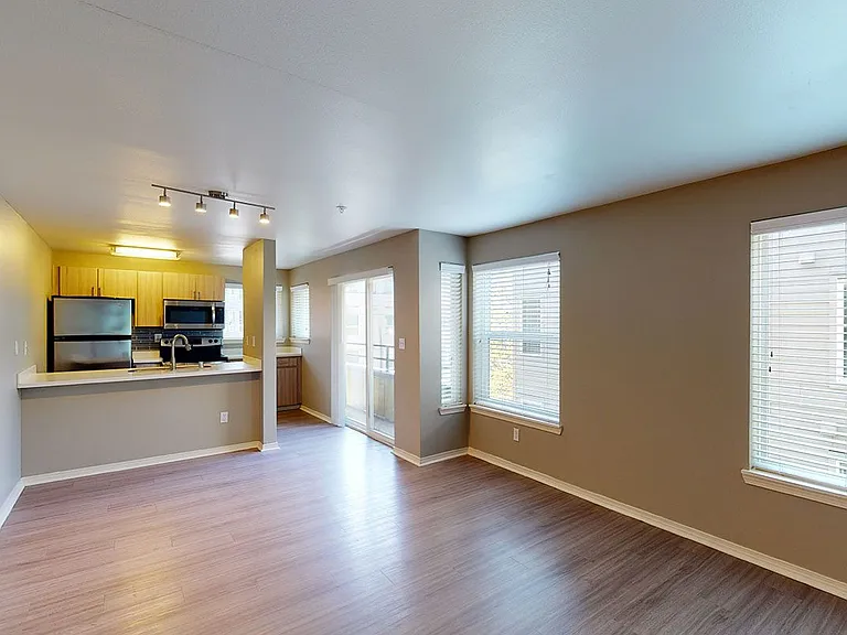 Apartment kitchen with stainless steel appliances, dining and living room with wood-style flooring.