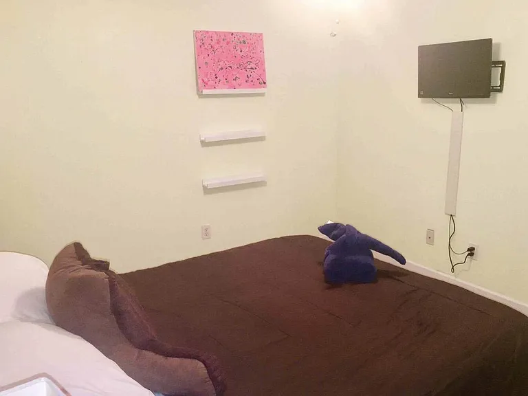 Bedroom with bed, wall-mounted TV, and floating shelves for display and small-item storage.